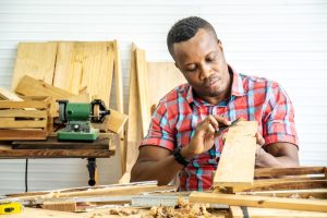 Services 7424164 jonge timmerman afrikaanse amerikaanse man kijken en kiezen hout en gebruiken schuurpapier te wrijven houten plank op werkplaats tafel in timmerman houtfabriek gratis foto